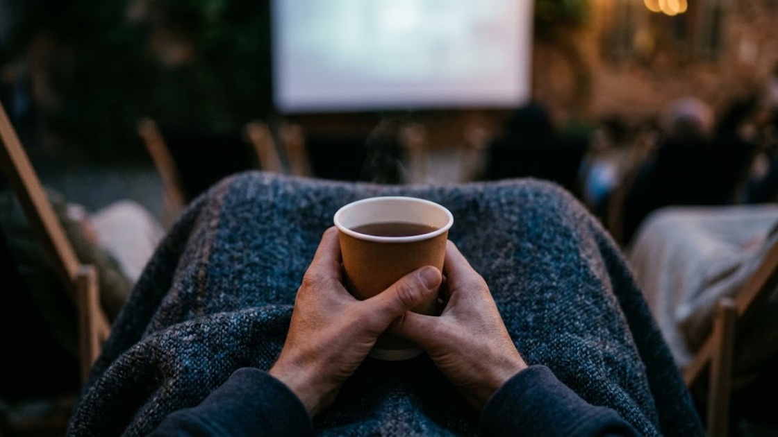 Hands holding a paper cup of tea over a wool blanket at a Berlin open air cinema in September