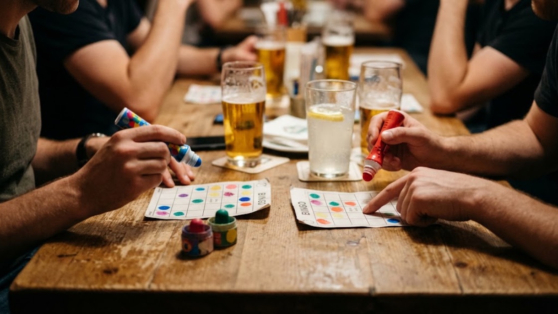 Close-up of two players marking paper bingo cards with dabber pens on a wooden bar table, one helping the other