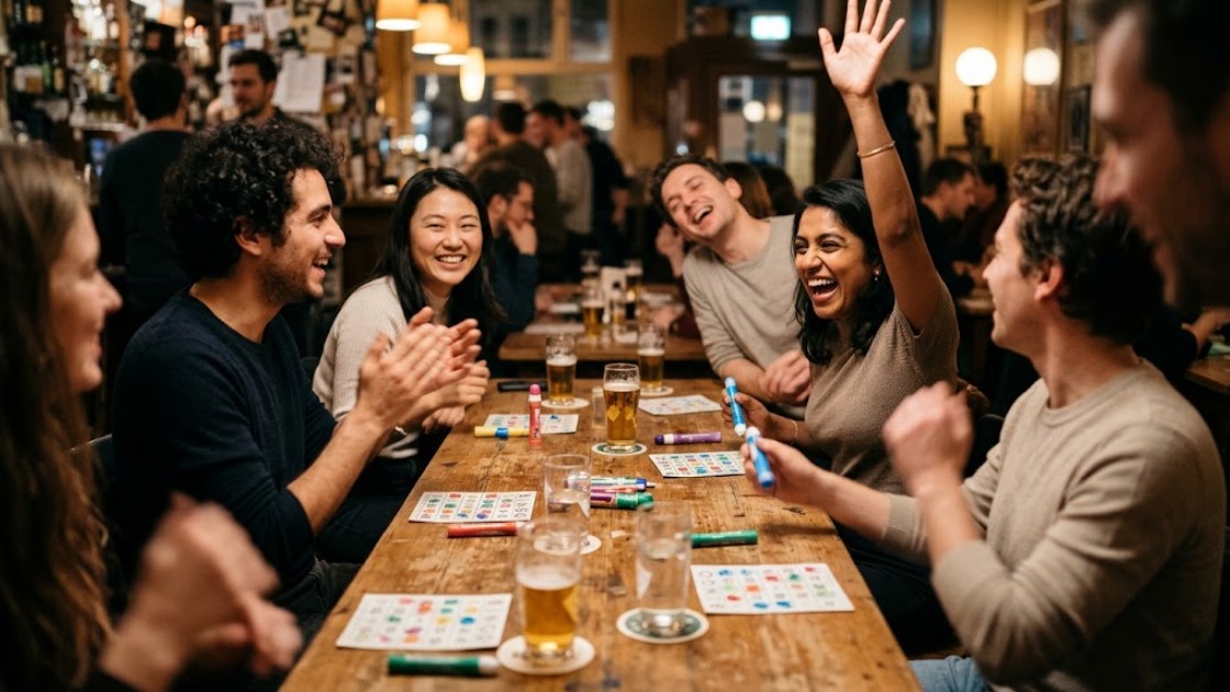 A table of friends and strangers cheering as one player raises her hand after winning a line at a Berlin bingo night