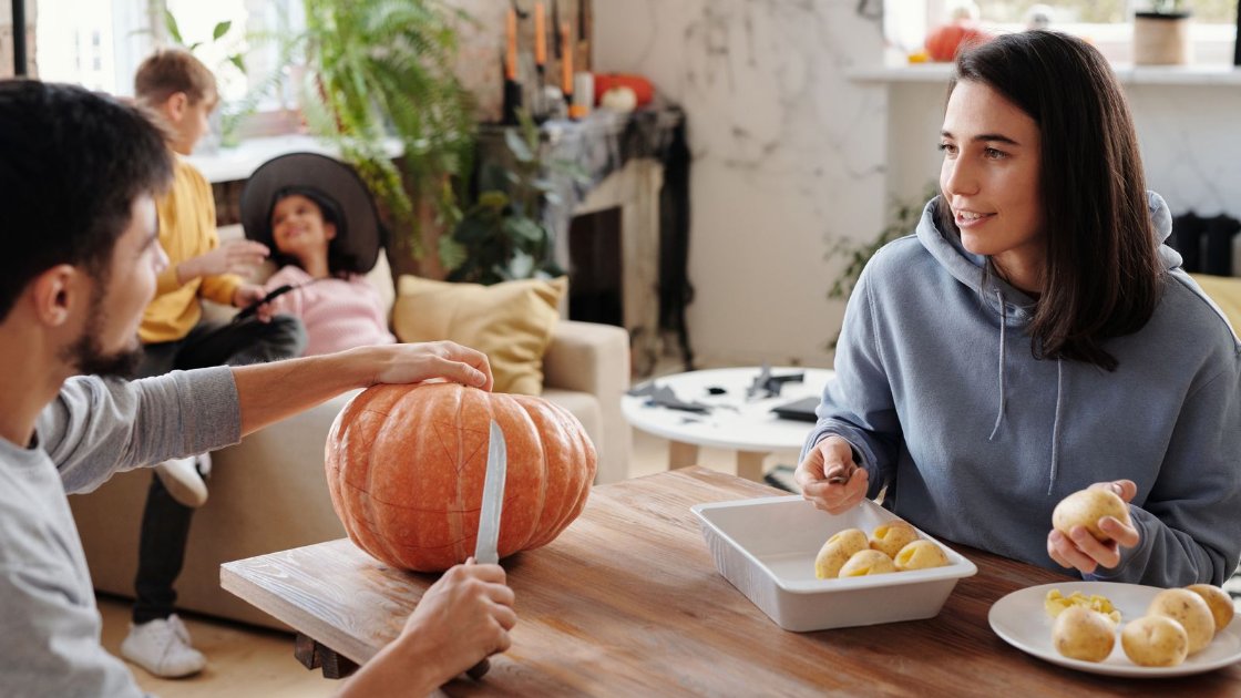 Couple carving a pumpkin at a wooden table in a bright flat