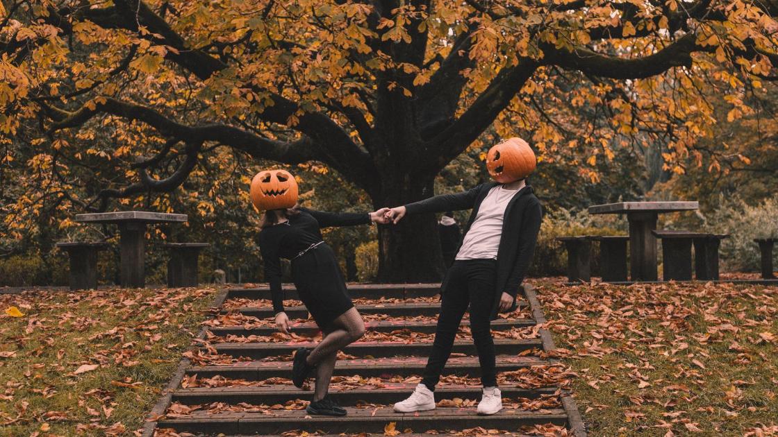 Halloween in Berlin 2026: two friends with pumpkin heads on autumn park steps