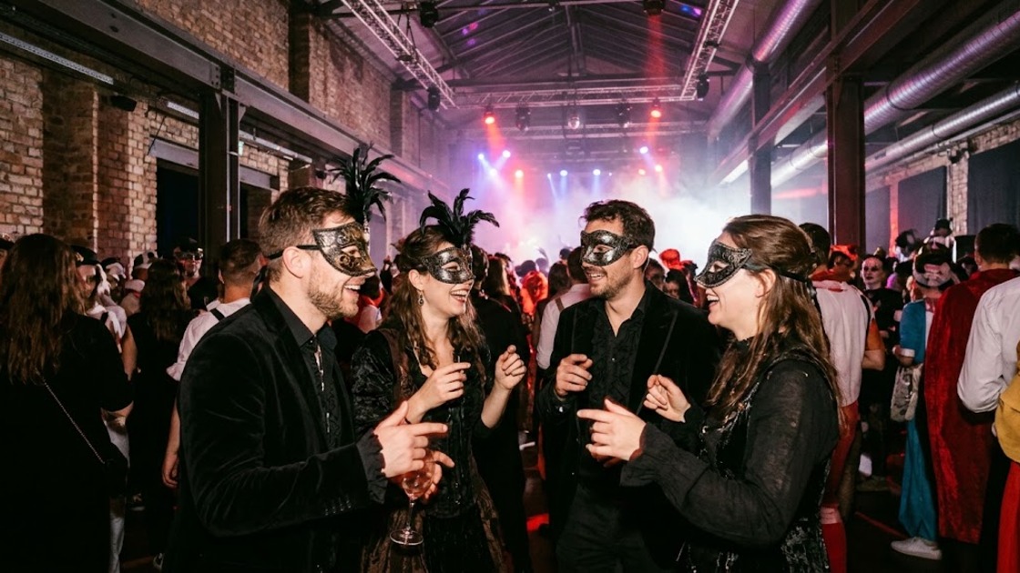 Four friends in masks and dark costumes dance at a Halloween masquerade in a Berlin club