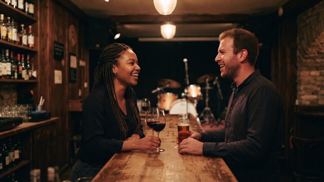 Two people chatting at a wooden bar between sets, a drum kit on the small stage behind them