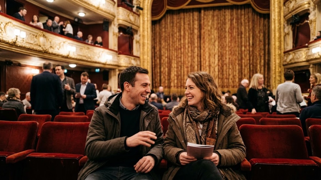 Two friends talk and laugh in red velvet seats during the interval of a musical